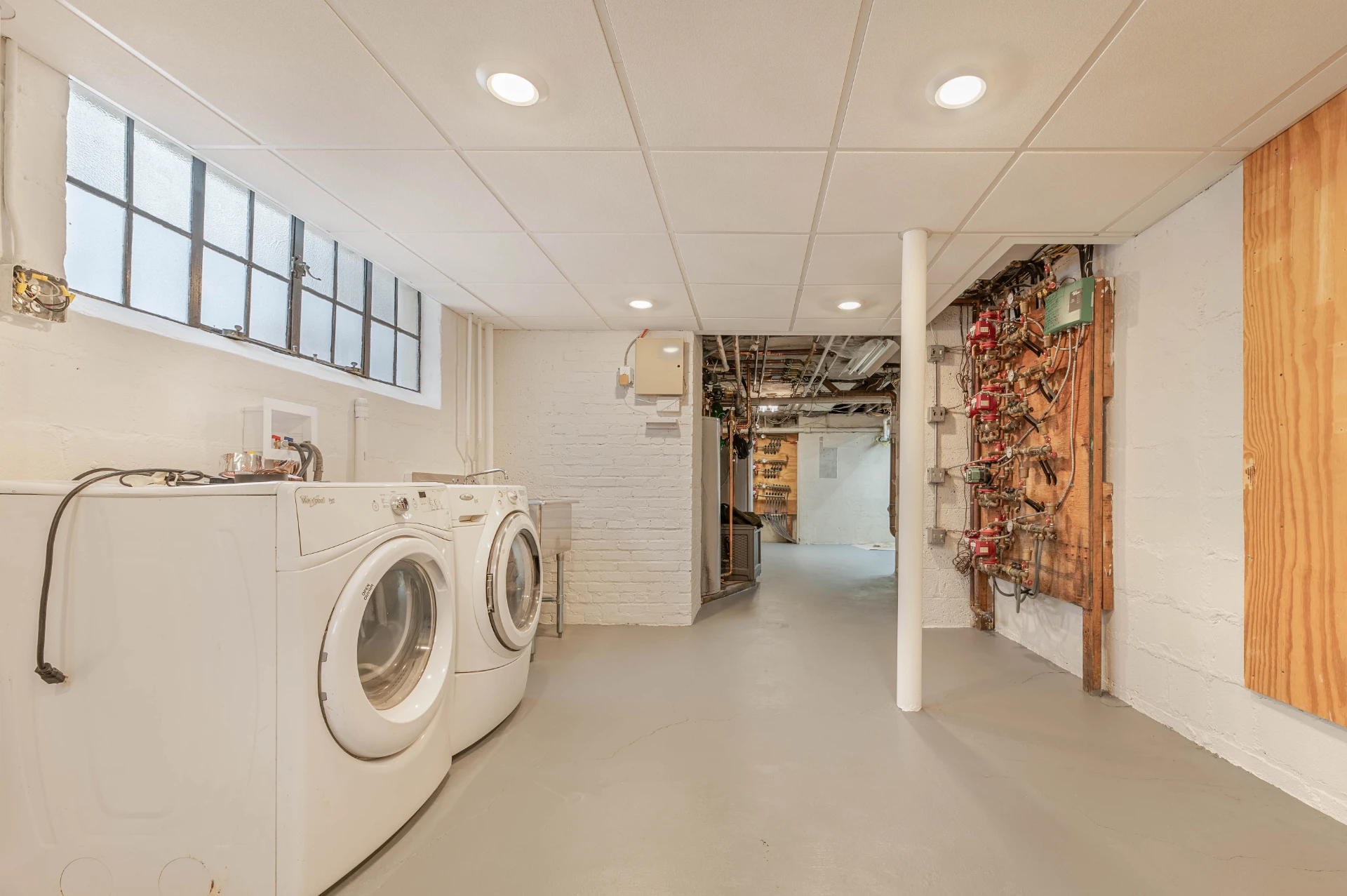 Finished basement with white painted brick, recessed lighting and a laundry area