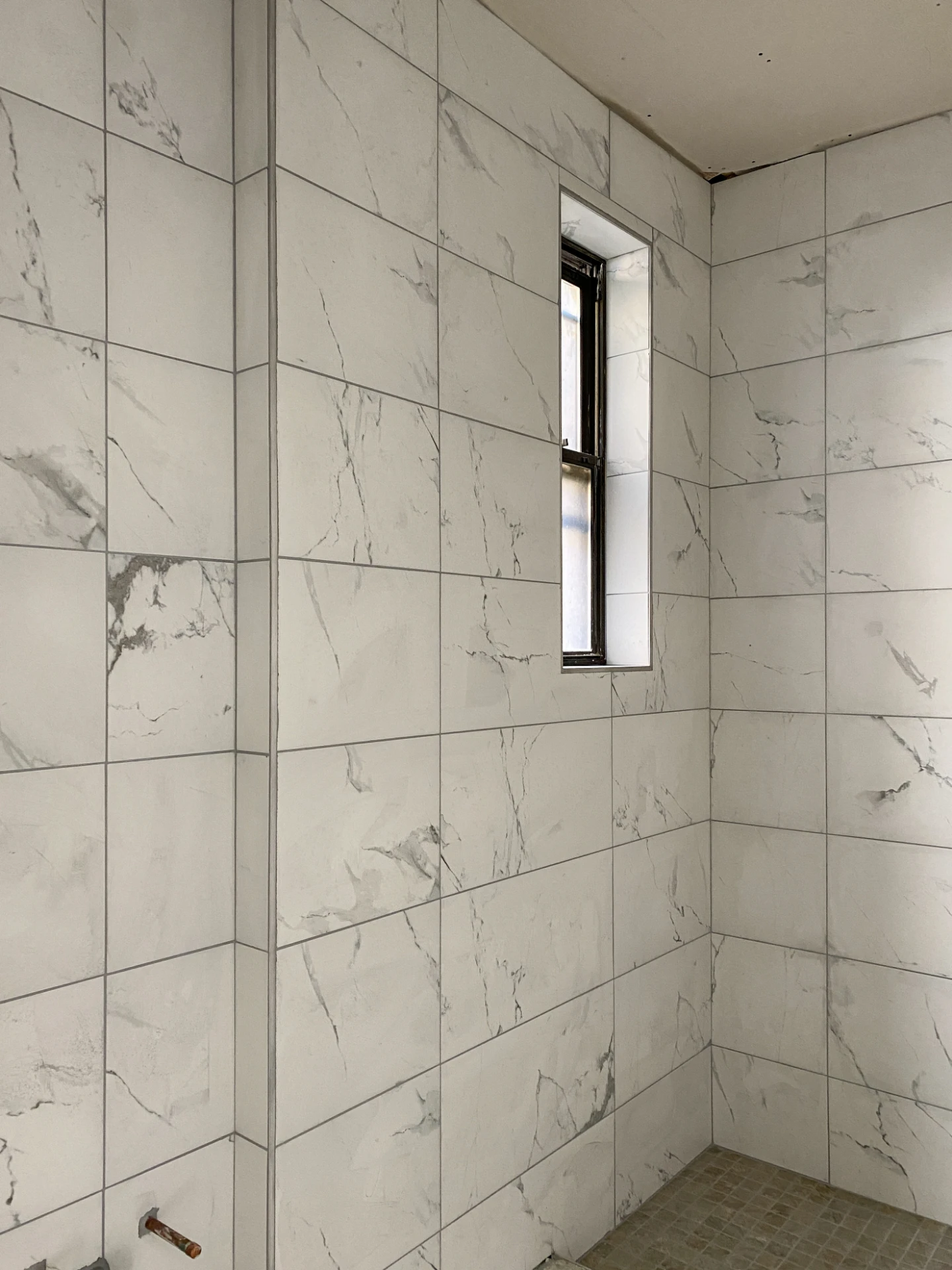 Finished bathroom in marble look tile with a narrow black framed window