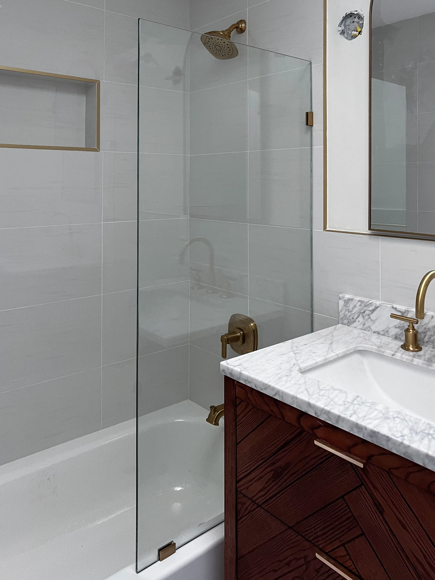Walk in shower with brass fixtures, a tiled niche and a brass framed mirror