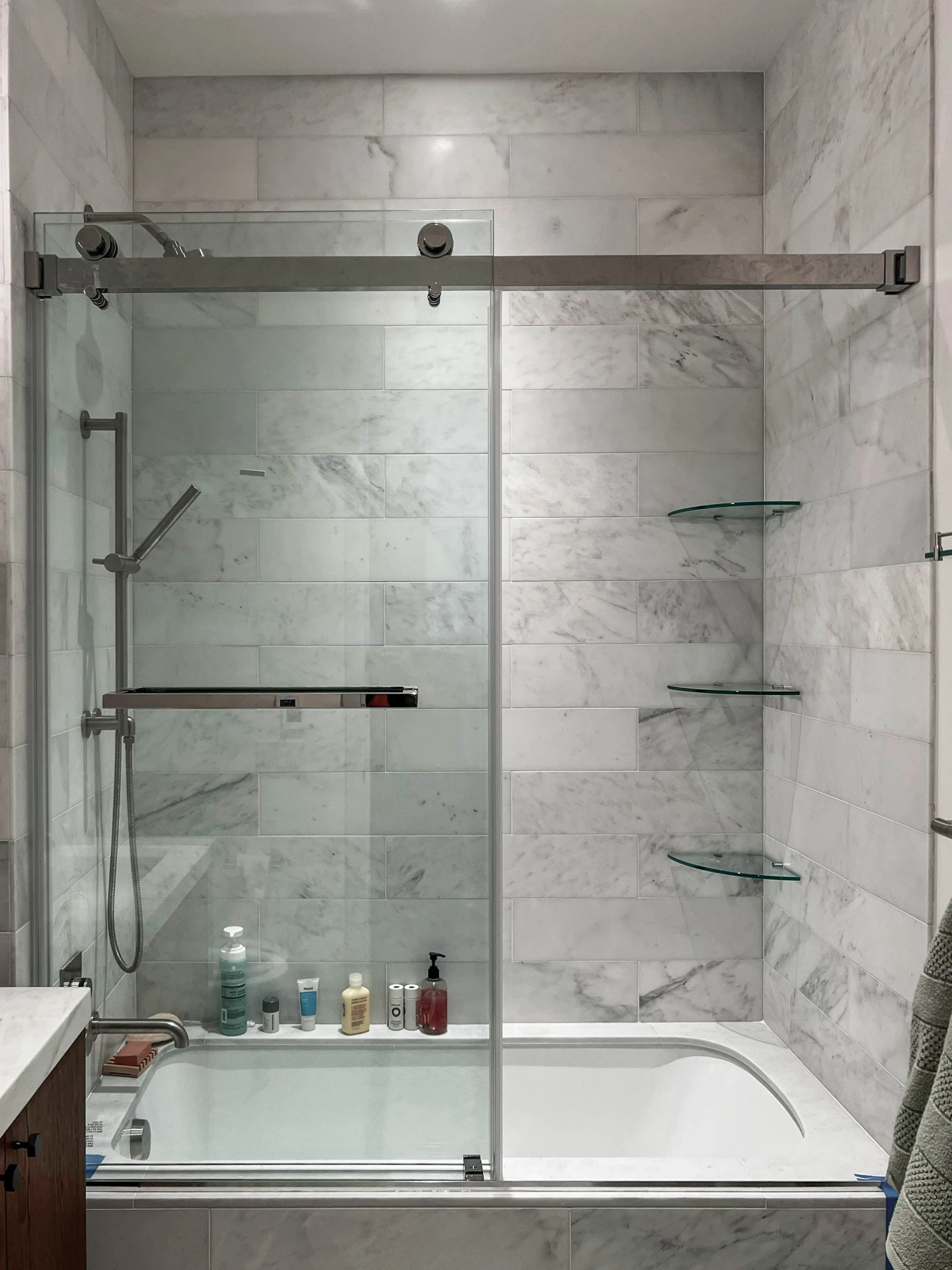 Finished marble shower with a sliding glass door and glass corner shelves
