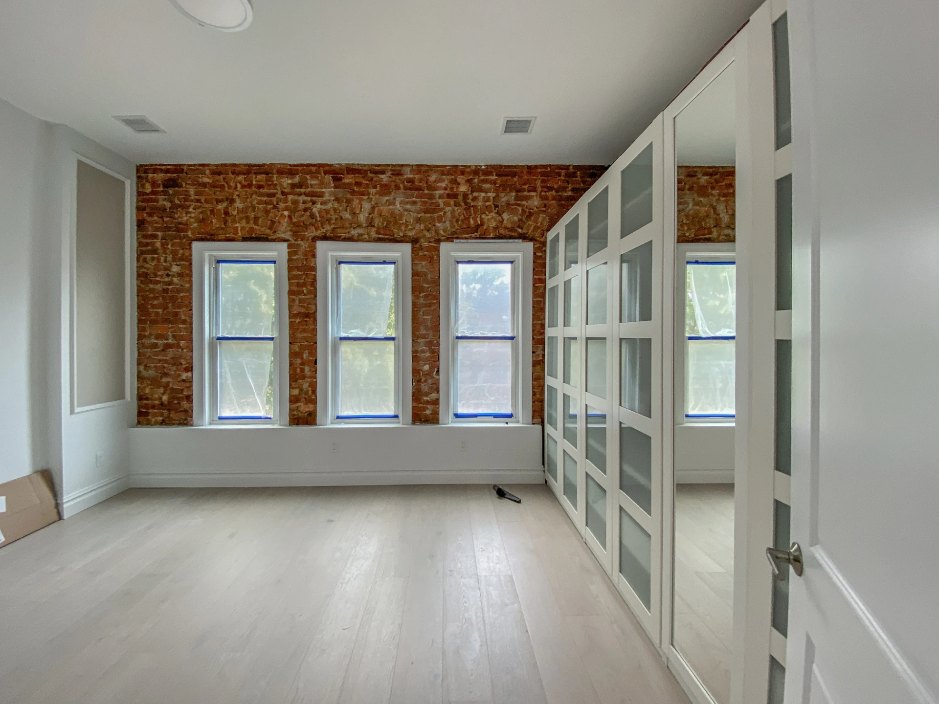 Wall of built in wardrobes with glass panelled doors beside exposed brick