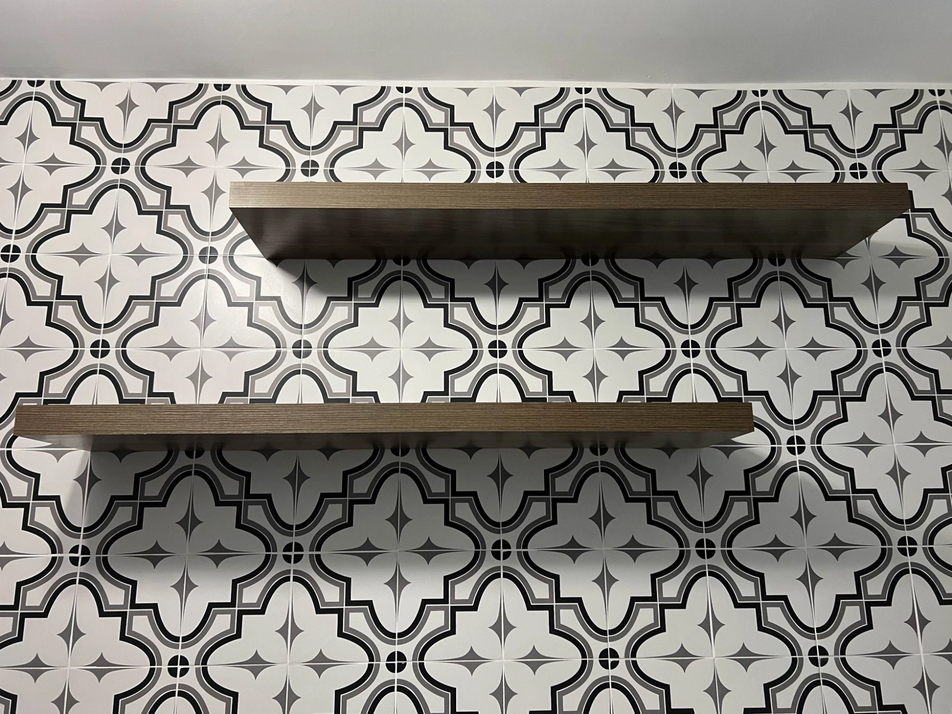 Two dark floating shelves mounted on patterned black and white tile