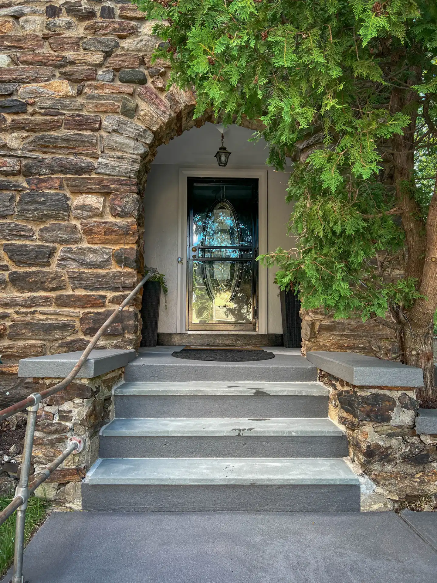 Stone archway entry with the front door set back under the trees