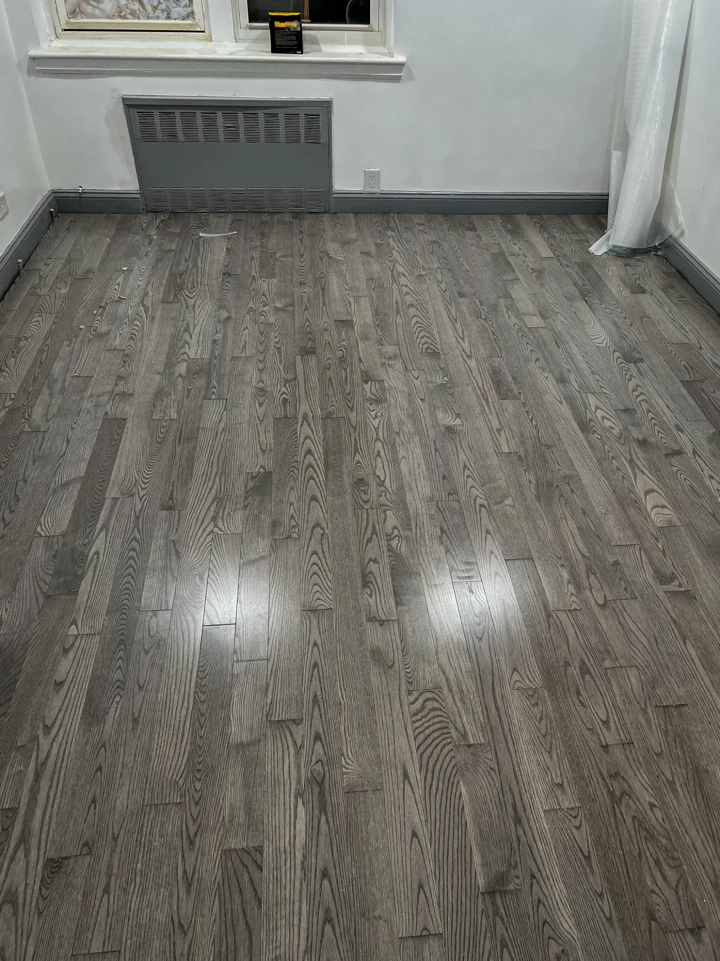 Finished grey toned wood floor in a cleared room with a radiator cover