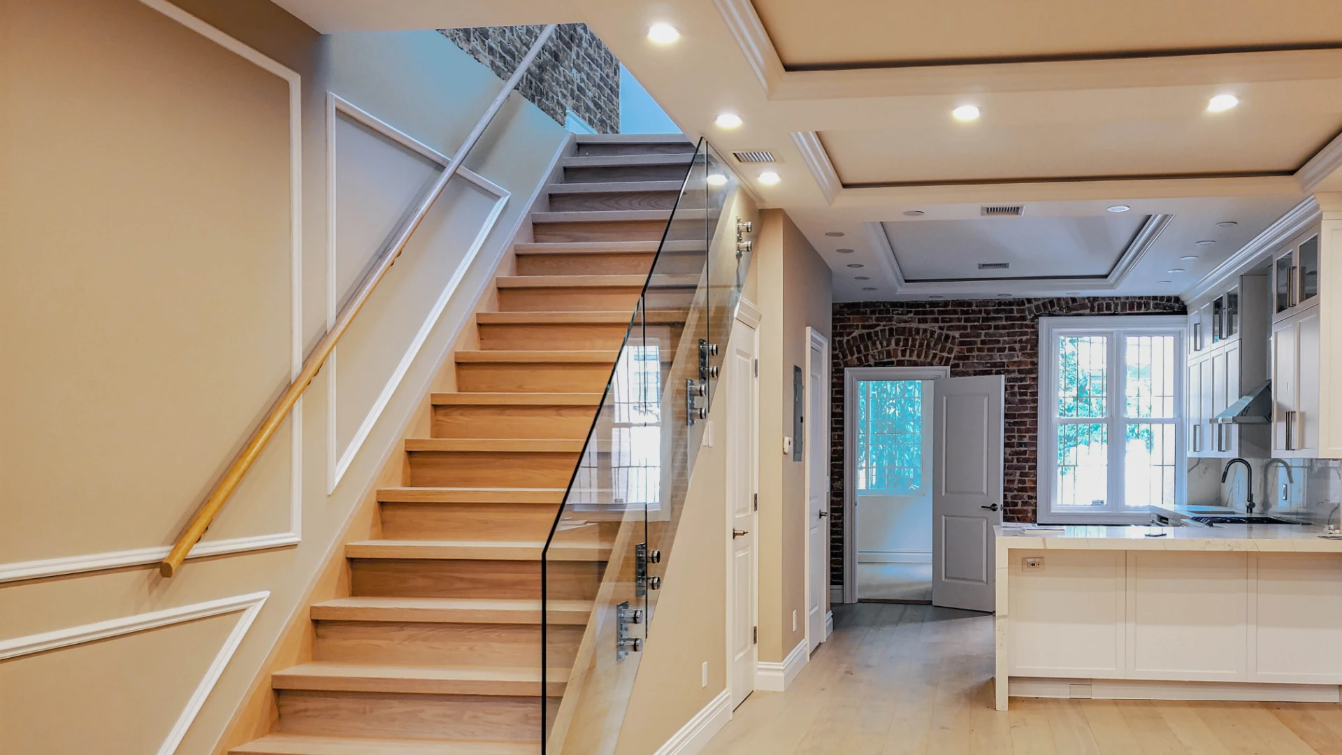 Open staircase with a glass railing beside a white kitchen
