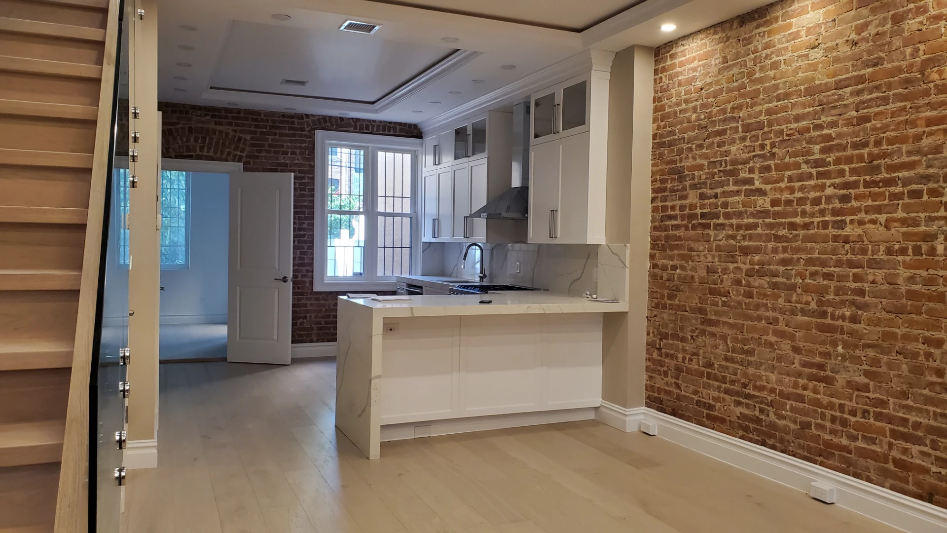 Open plan kitchen with exposed brick, wood floors and a glass stair railing
