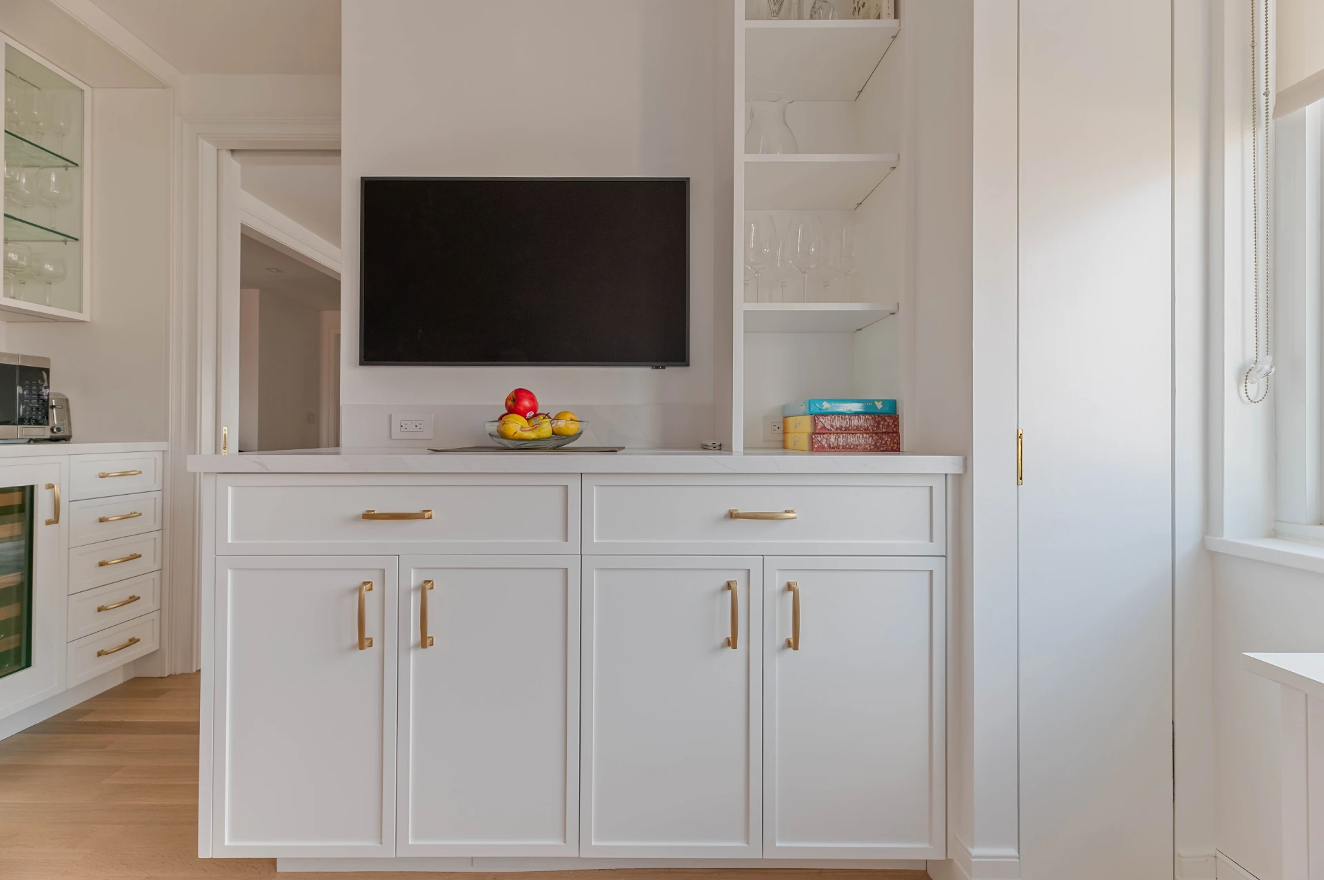 Built in cabinetry with a television niche, brass pulls and open shelving