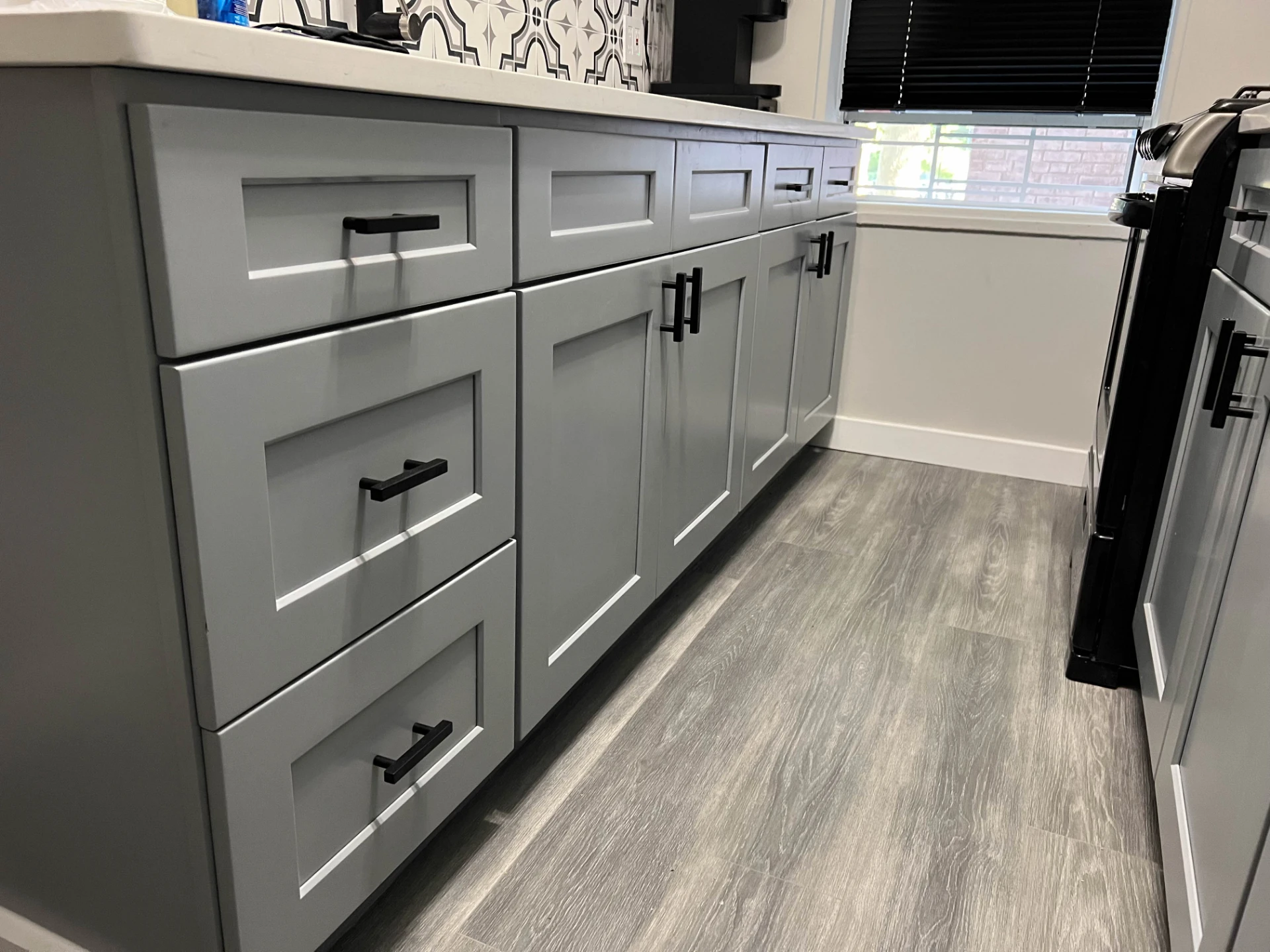 Run of grey shaker cabinets with black pulls over wood look flooring