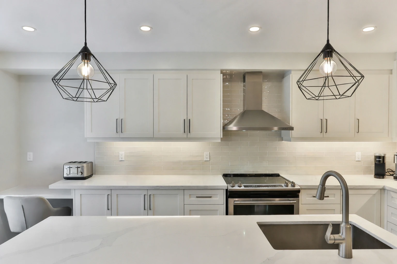 Finished white kitchen with a range hood, pendant lights and a quartz island