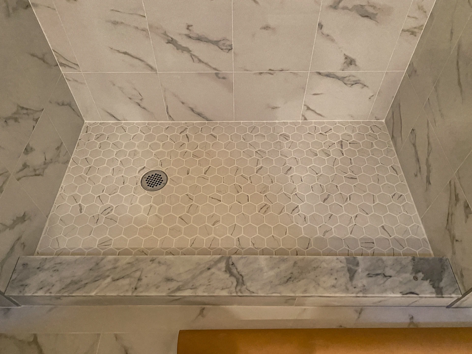 Finished shower pan in hexagonal mosaic tile with marble look walls